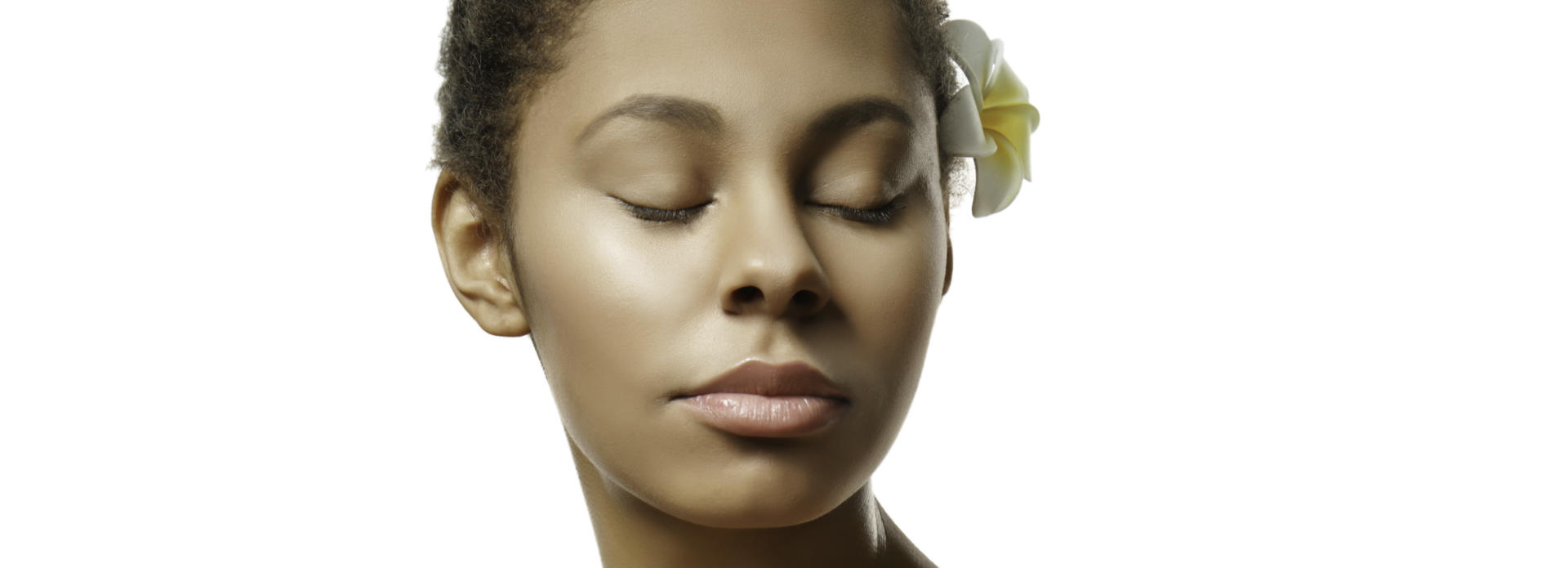 Youthful smooth face of an Afro-American woman with closed eyes and a flower behind her left ear.