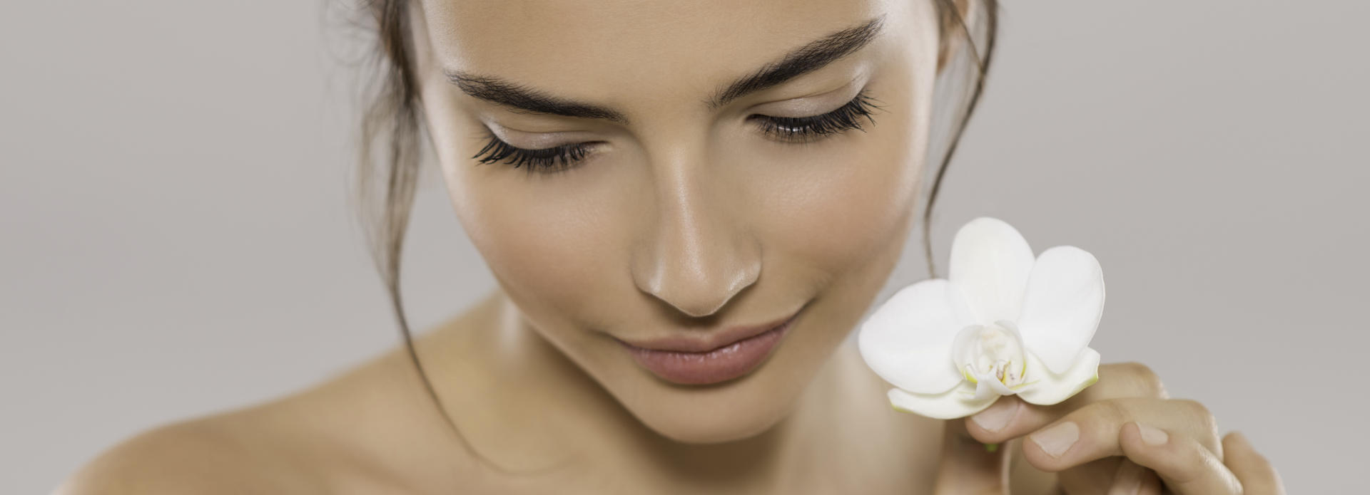 Woman with perfect skin due to laser treatments holding a flower near her face.