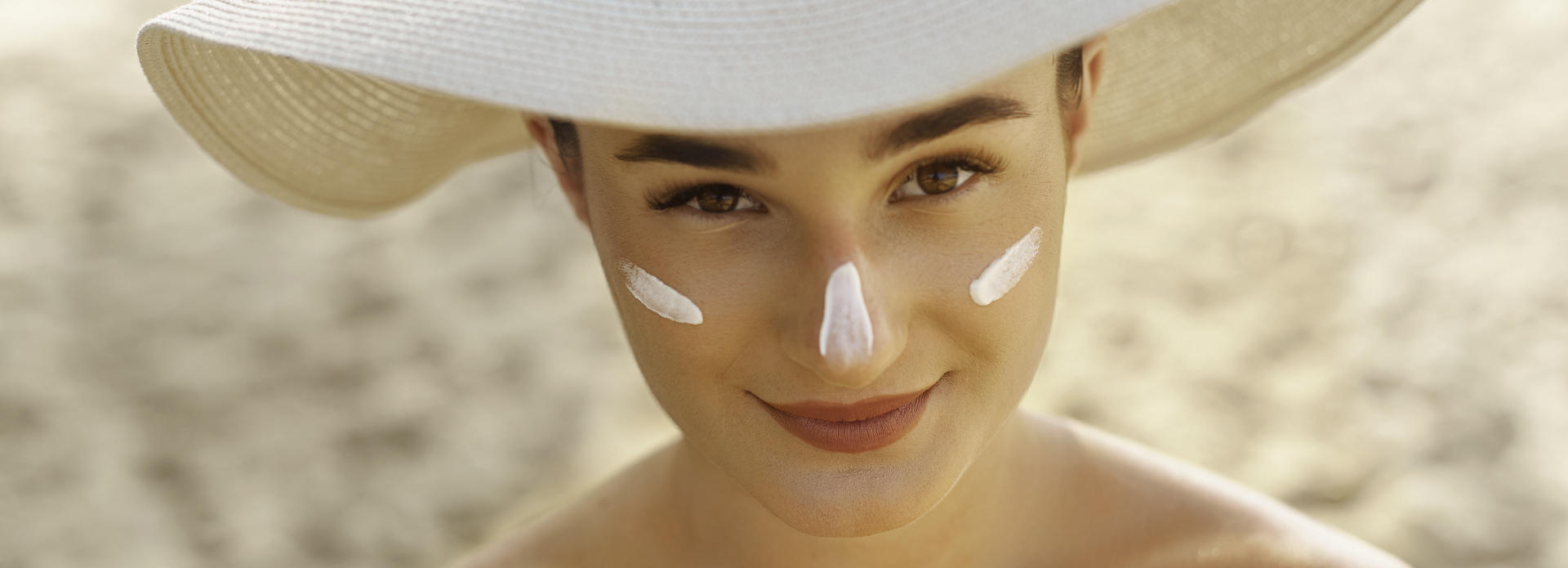 Sunbathing young woman with sunscreen on her face wearing a hat to protect from the sun.