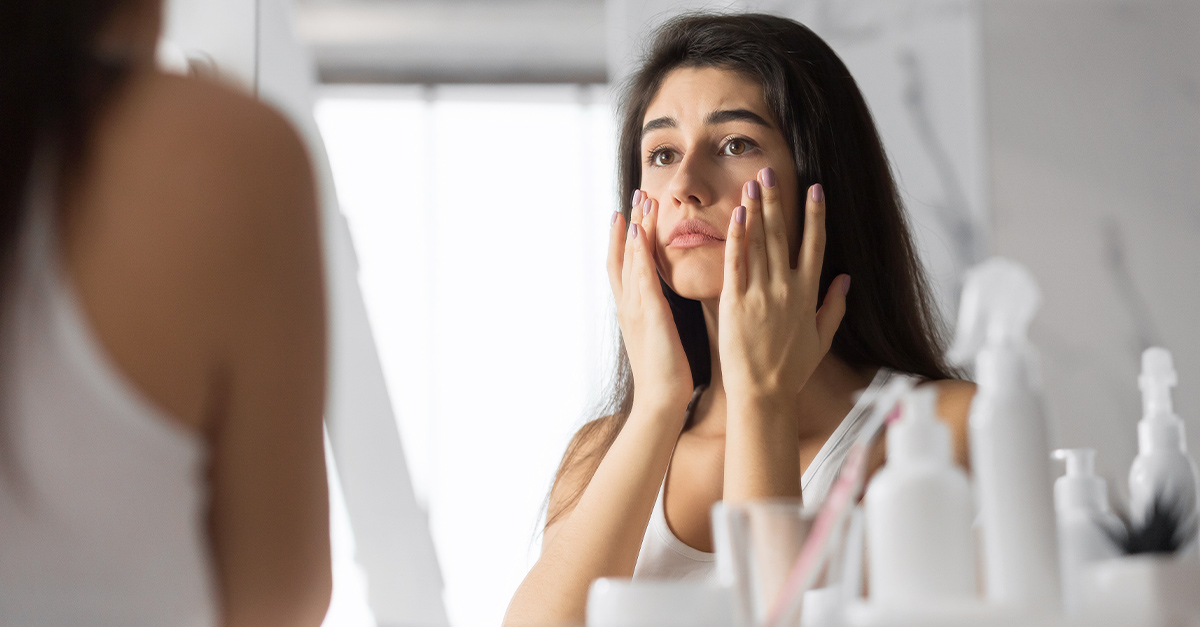 Female touching face looking sad in mirror.
